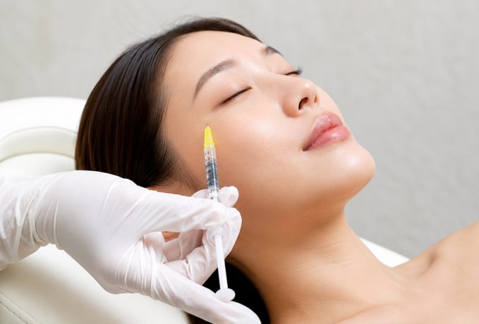 A close-up of a woman receiving a dermal filler injection near her eye, with a gloved hand administering the procedure.